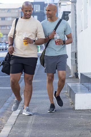 African american friends walking and chatting on urban sidewalk with drinks in daylight