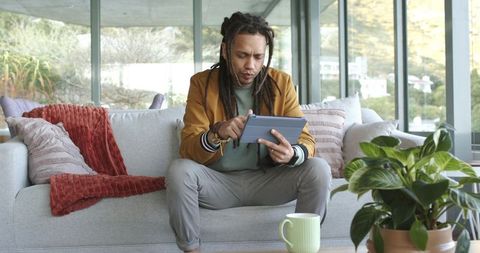 Man using tablet on modern living room sofa focusing on remote work and productivity