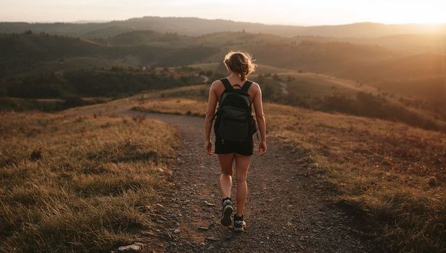 Solo female hiker walking golden-hour ridge trail with backpack
