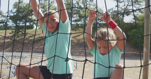 Two determined caucasian girls climbing nets on bootcamp training course. Fitness, childhood, challenge and healthy lifestyle.