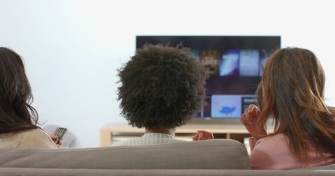 Multiracial women watching streaming tv on gray sofa enjoying relaxed movie night at home