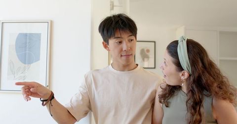 Young couple discussing home decor, man pointing and woman reacting during home tour