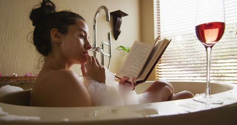 Woman Relaxing in Bathtub with Book and Wine in Peaceful Atmosphere