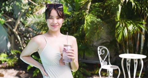 Smiling Woman Enjoying Refreshing Drink in Tropical Garden