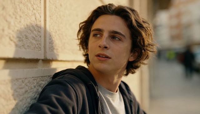 Young man leaning on textured wall looking thoughtful while strolling sunlit urban street