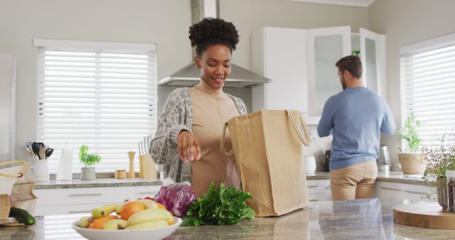 Image of african american woman unpacking groceries in kitchen. Love, relationship and spending quality time together at home.
