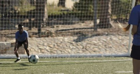Youth goalkeeper crouching to save soccer ball on turf during outdoor practice