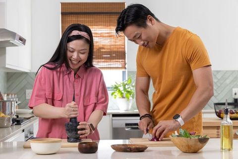 Asian couple cooking at kitchen island, woman using mortar and pestle, man slicing onion