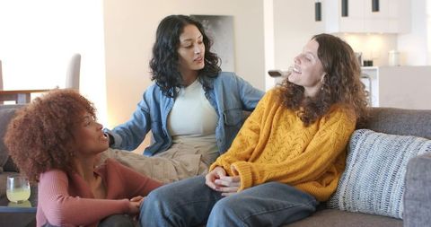 Female friends chatting on gray sofa in open-plan living room, casual cozy home gathering