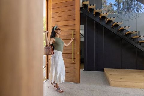 African american woman entering modern home through oversized wooden door with brass pull