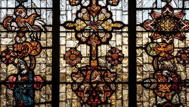 Ornate stained glass window with cross motif and sunlit illumination