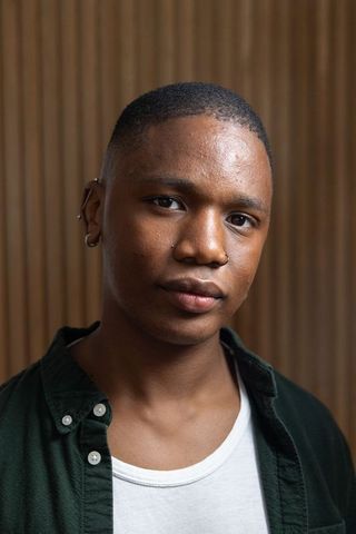 African american young man looking at camera wearing nose hoop and earrings on wood slats