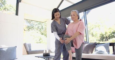 Physical Therapist Assisting Senior Woman with Home Leg Exercises