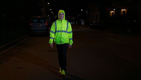Pedestrian walking in neon reflective hi-vis jacket on dark urban street at night