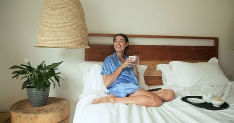Woman Relaxing in Pajamas on Cozy Bed Enjoying Morning Coffee
