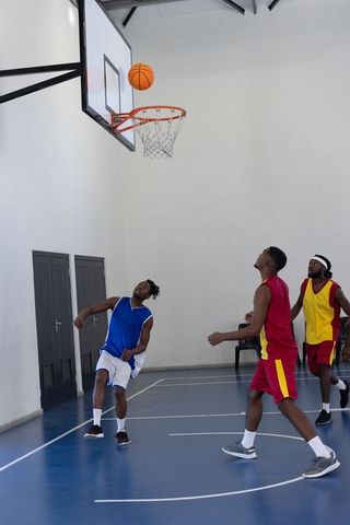 Basketball Players Competing Indoors Reaching Near Hoop