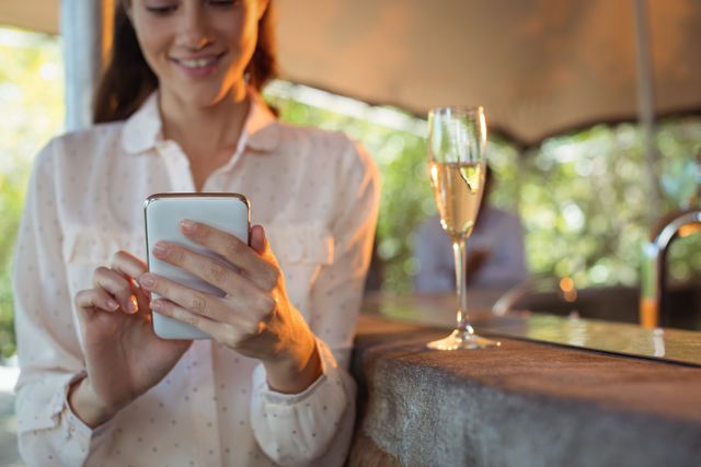 Smiling woman using mobile phone while having a glass of champagne in restaurant