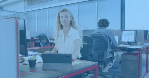 Female professional tapping tablet at minimalist coworking desk, open-plan productivity