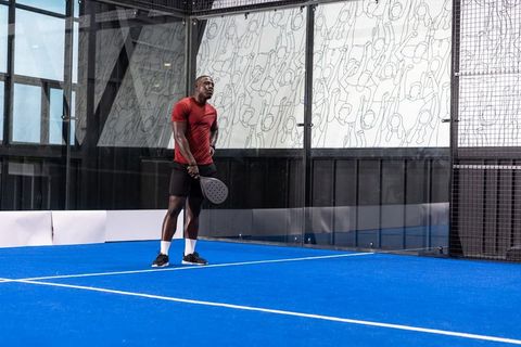 African american male athlete playing padel on indoor blue court preparing to serve
