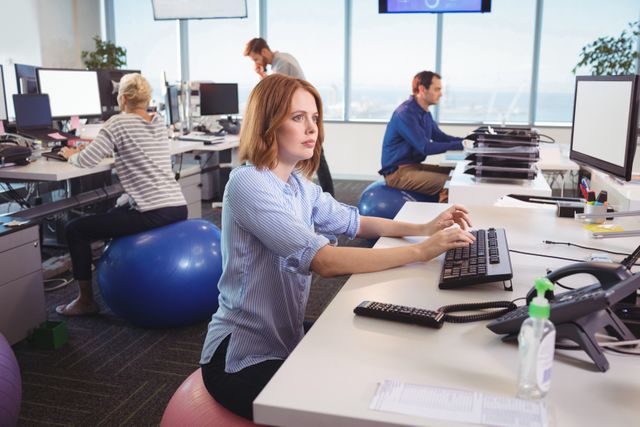 Thoughtful businesswoman sitting on exercise ball at desk in office