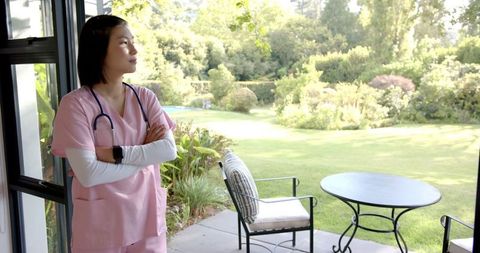 Thoughtful Nurse in Pink Scrubs Looking at Lush Garden