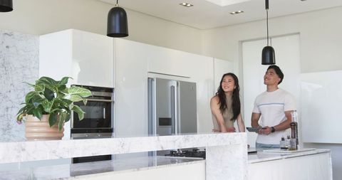 Diverse Couple Smiling in Bright Modern Marble Kitchen Holding Tablet, Looking Up