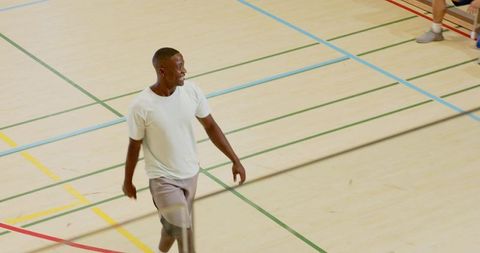 Adult man walking across indoor gym court with colorful floor markings and sneakers