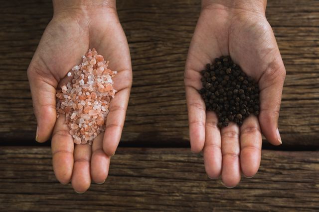 Close-up of hands holding sea salt and black pepper seeds
