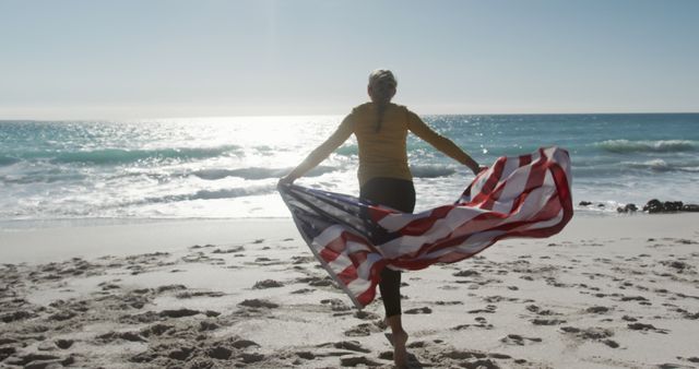 Woman running on beach with American flag creates a sense of freedom and celebration. Perfect for depicting themes of patriotism, outdoor activities, holidays like Independence Day or Memorial Day, and joyful lifestyles. Ideal for travel advertisements, patriotic campaigns, and lifestyle blog visuals.