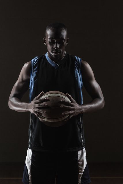 This image captures a basketball player holding a ball in a gym, exuding focus and determination. Ideal for use in sports-related content, fitness promotions, motivational posters, and athletic training materials.