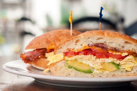 Serving breakfast sandwich with scrambled eggs, avocado, tomato and crispy bacon
