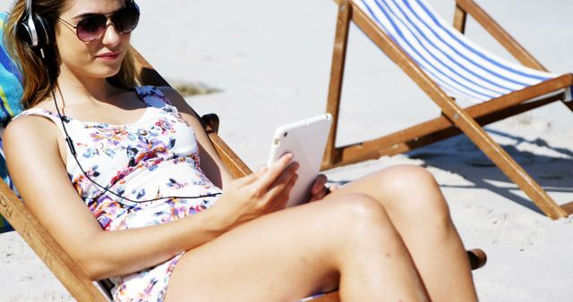 A young Caucasian woman relaxes on a beach chair using her smartphone, with copy space. She enjoys a sunny day at the beach, combining leisure with connectivity.