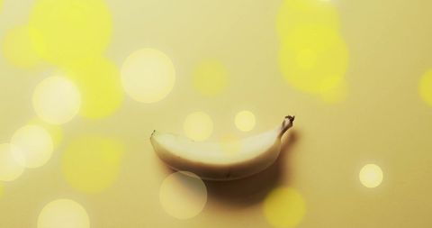 Single banana placed on vibrant yellow background enhanced with ethereal light spots creating luminous effect. Perfect for themes related to fruity and whimsical mood. Useful for healthy dietary articles, food blogs, commercial display in fruit markets, or illustrations promoting vibrant health.