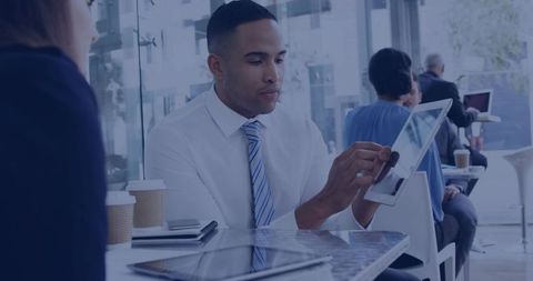 Businessman in white shirt and striped tie tapping tablet in modern cafe coworking meeting