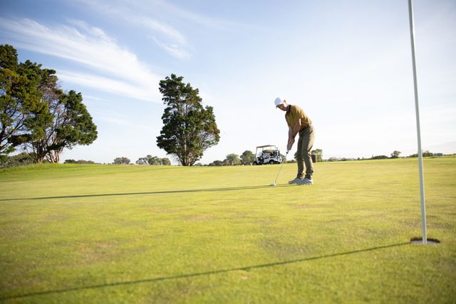 Caucasian male golfer practicing on a golf course on a sunny day wearing a cap and golf clothes, hitting a golf ball. Hobby healthy lifestyle leisure.