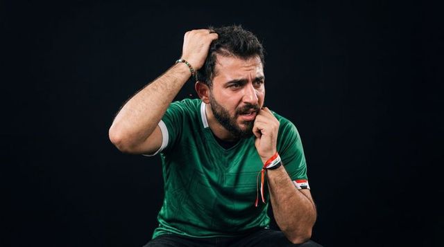 Anxious football fan holding head and pressing temple wearing green jersey with wristbands