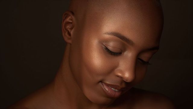 Shaved-head woman tilting head down, closing eyes, smiling, radiant skincare portrait