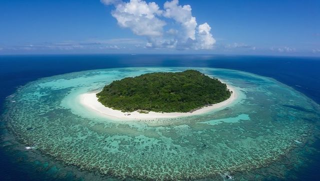 Secluded tropical island ringed by turquoise lagoon and coral reef with white sandy beach