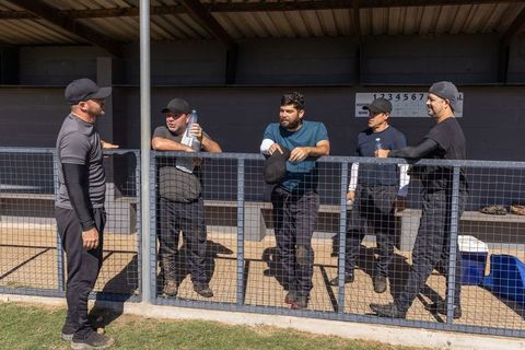 Sunlit baseball teammates chatting and resting in dugout leaning on fence after inning