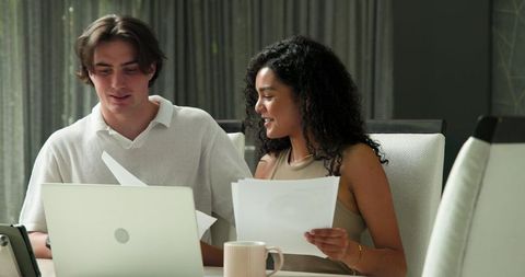 Multiracial couple checking documents together in bright living room