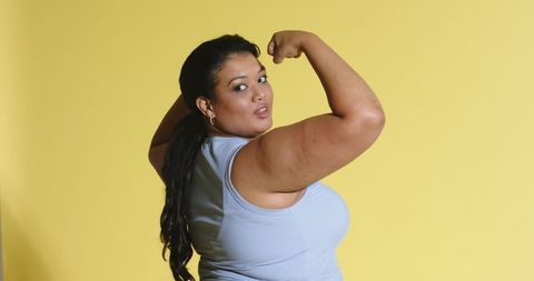 Curvy woman flexing bicep showing confidence and strength on yellow backdrop