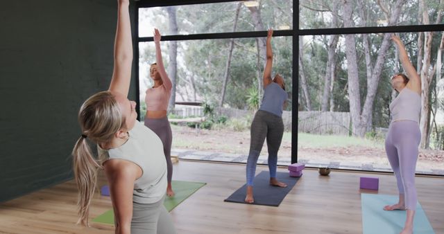Women in a yoga studio with large windows, performing various stretching exercises together. Great for fitness-related content, yoga workshop promotions, healthy lifestyle blogs, and wellness product advertisements.