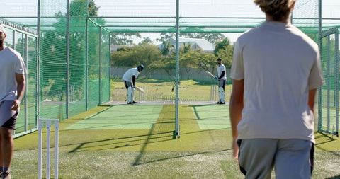 Cricket players practicing in outdoor net lanes swinging bats on synthetic turf training