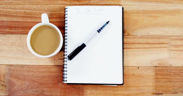 A cup of coffee sits next to a 'To Do List' notepad and a pen on a wooden surface, with copy space. It suggests a moment of planning or organization, at the start of a busy day.