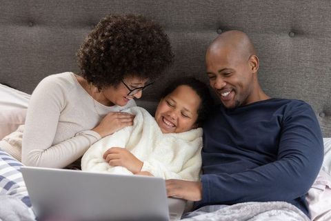 Cozy family cuddling on bed using laptop, parents and child sharing screen time