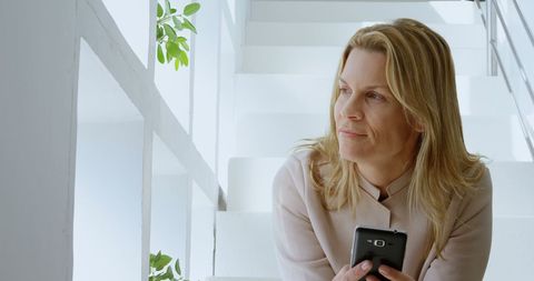Woman Holding Mobile Phone Thoughtfully on Stairs