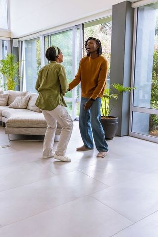 Couple dancing in sunlit modern living room with glass walls and plants in casual clothes