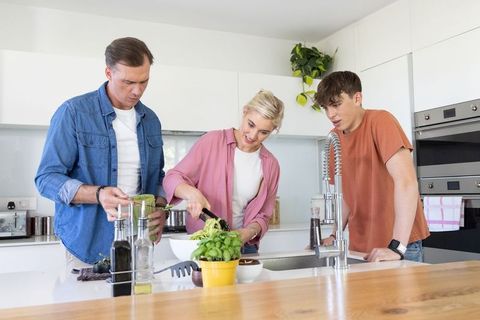 Family preparing healthy green salad together at kitchen island in modern home