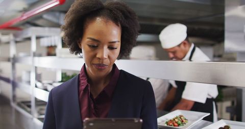 Female manager using tablet in busy restaurant kitchen