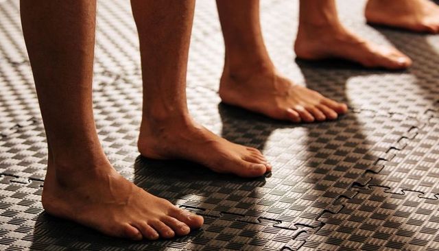 Barefoot athletes standing in line on black foam gym mat closeup of feet and ankles